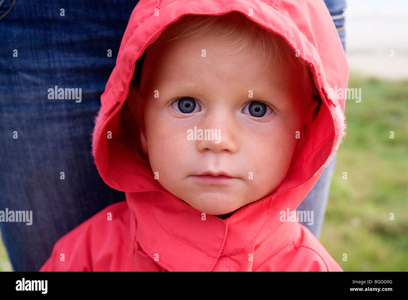 Portrait of a little girl with a red rain jacket, her mother behind her Stock Photo