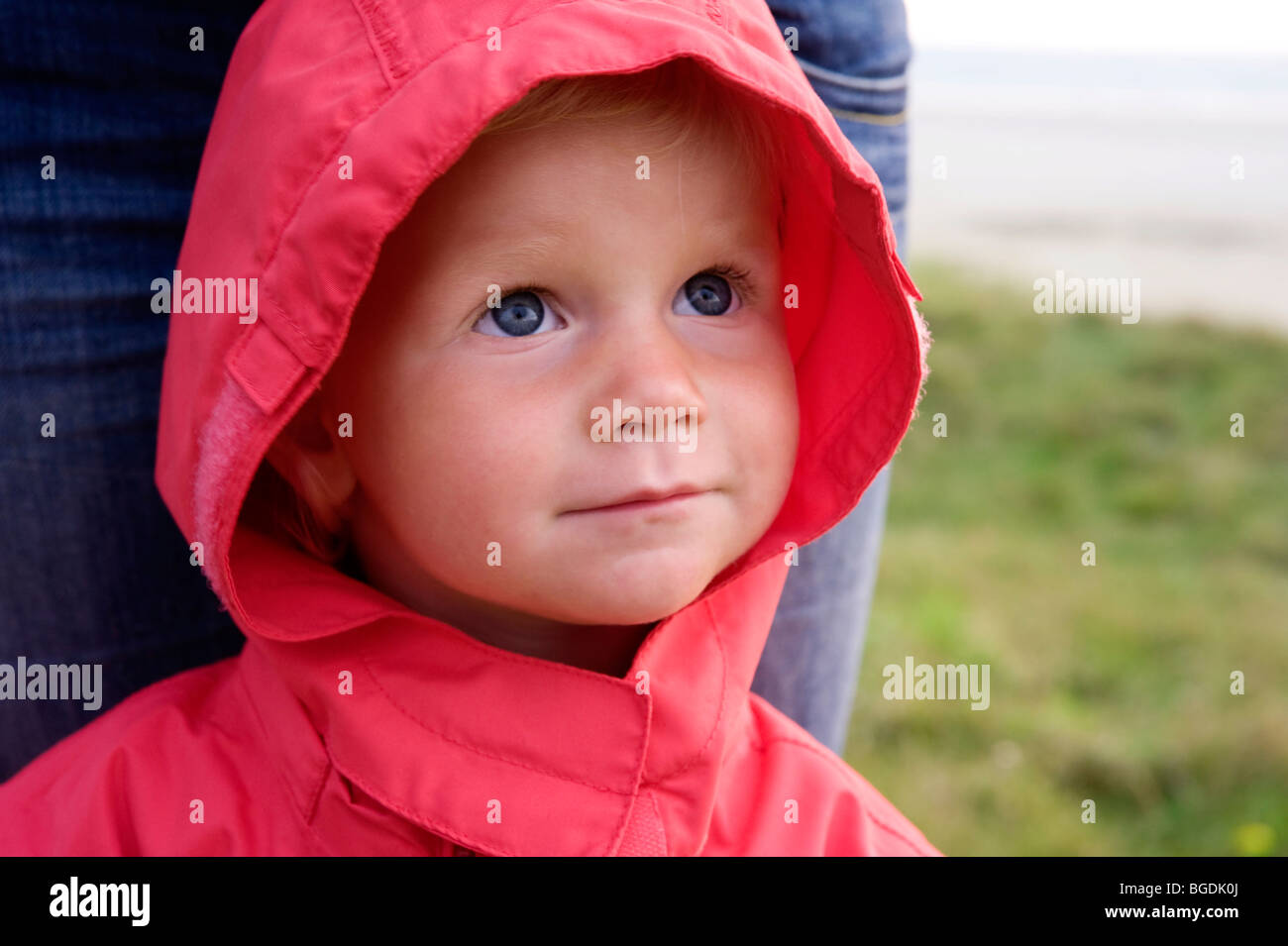 Portrait of a little girl with a red rain jacket, her mother behind her Stock Photo