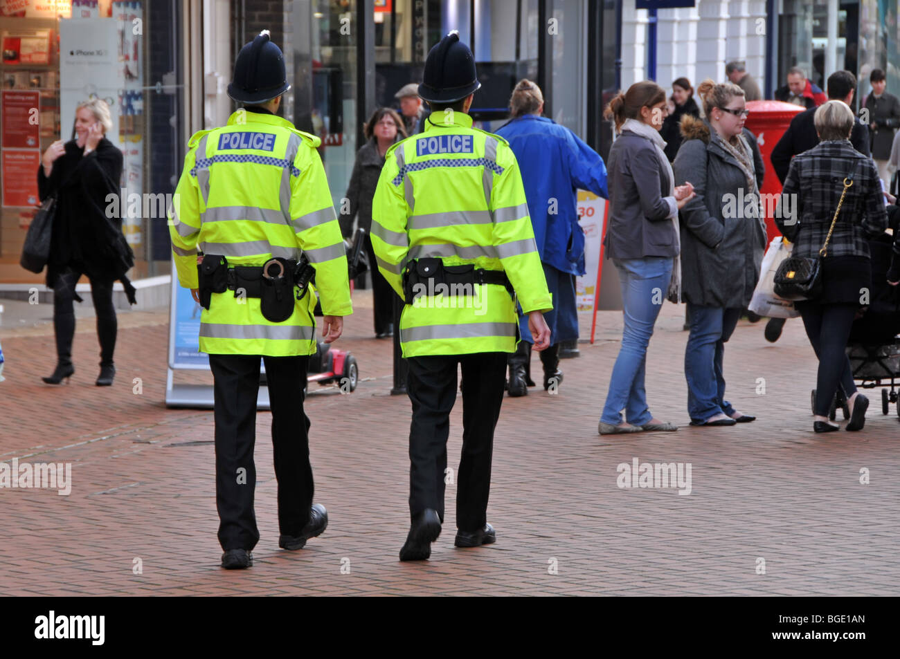Police officers back view two of a kind policemen on foot patrol walking along busy shopping high street in City of Chelmsford Essex England UK Stock Photo