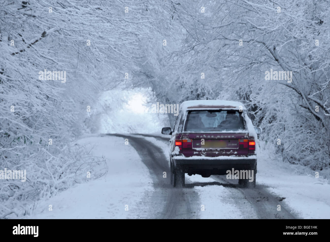 Snow scene back rear view Range Rover car driving country road lane below tunnel of snow covered trees in winter wonderland Brentwood Essex England UK Stock Photo