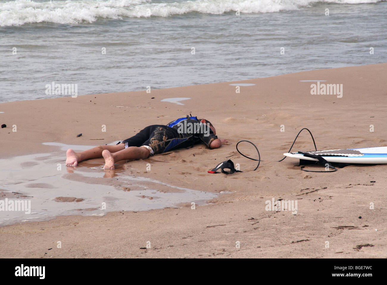 Small surfer exhausted and sleeping on beach near surf Stock Photo
