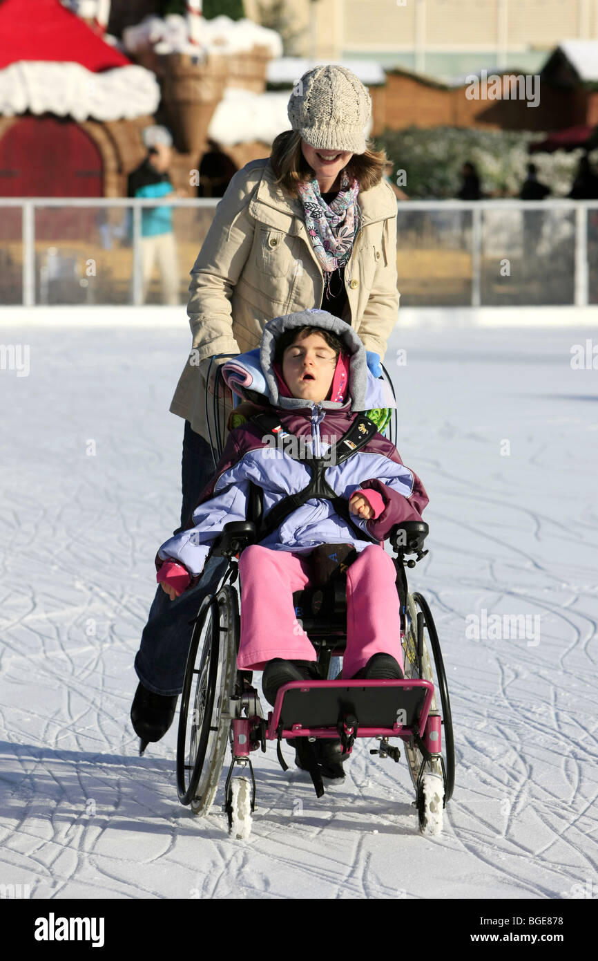 Disabled child in a wheelchair being pushed around an ice rink by a