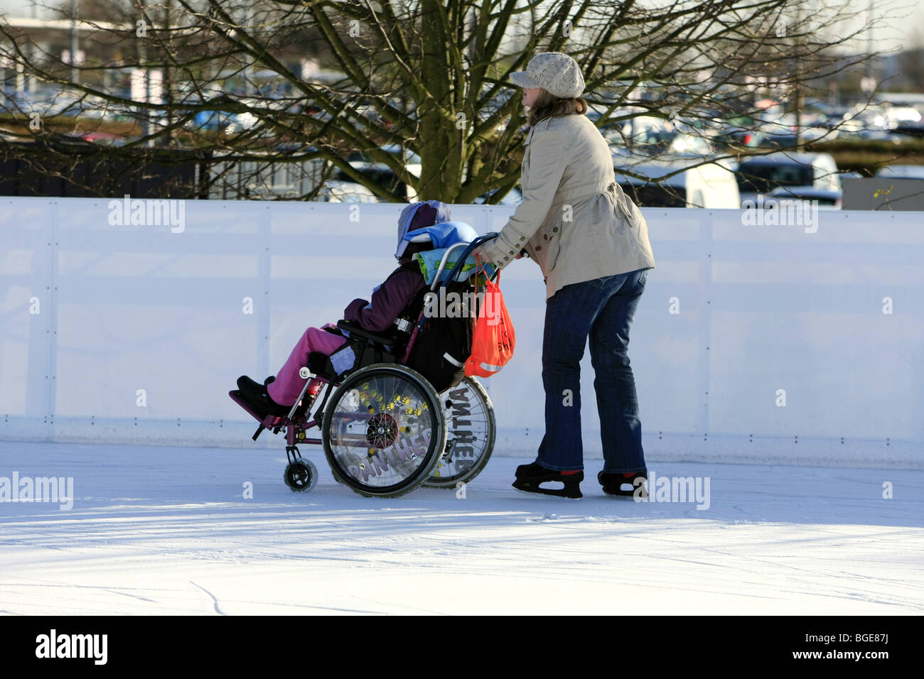 Disabled child in a wheelchair being pushed around an ice rink by a carer on a winter day out