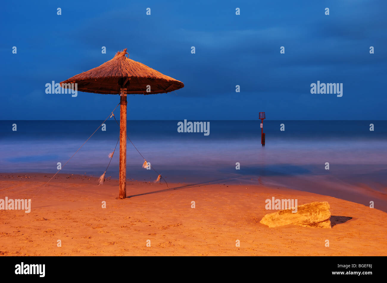A Hawaiian Grass parasol on the beach in Swanage, Dorset - shot at dusk. Stock Photo