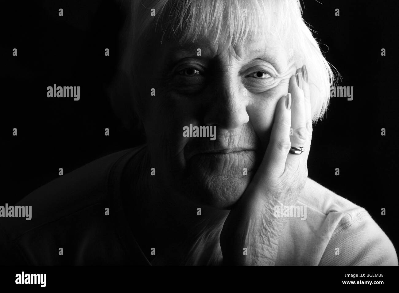 an elderly senior beautiful woman looks on in a low key dramatic setting Stock Photo