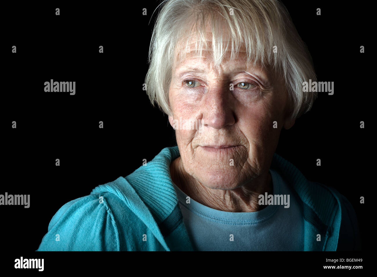 an elderly senior beautiful woman looks on in a low key dramatic setting Stock Photo