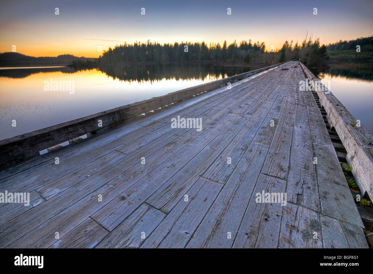 Old wooden bridge spanning the entrance to Clayoquot Arm of Kennedy Lake at sunset, a transition area of the Clayoquot Sound UNE Stock Photo