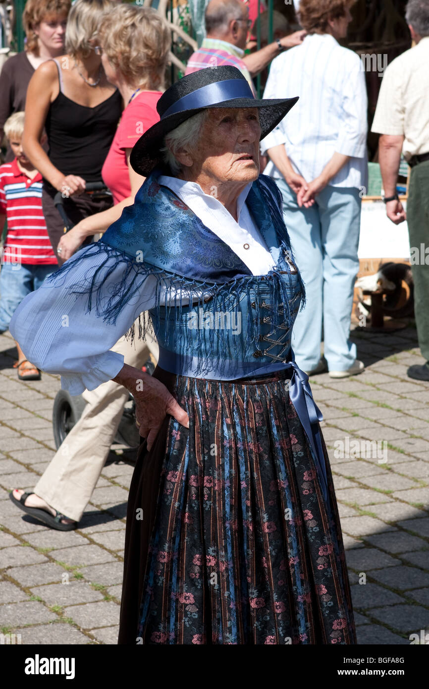 Old woman standing having her hands on her waist as tourists roaming in the market in Bavaria, Germany Stock Photo