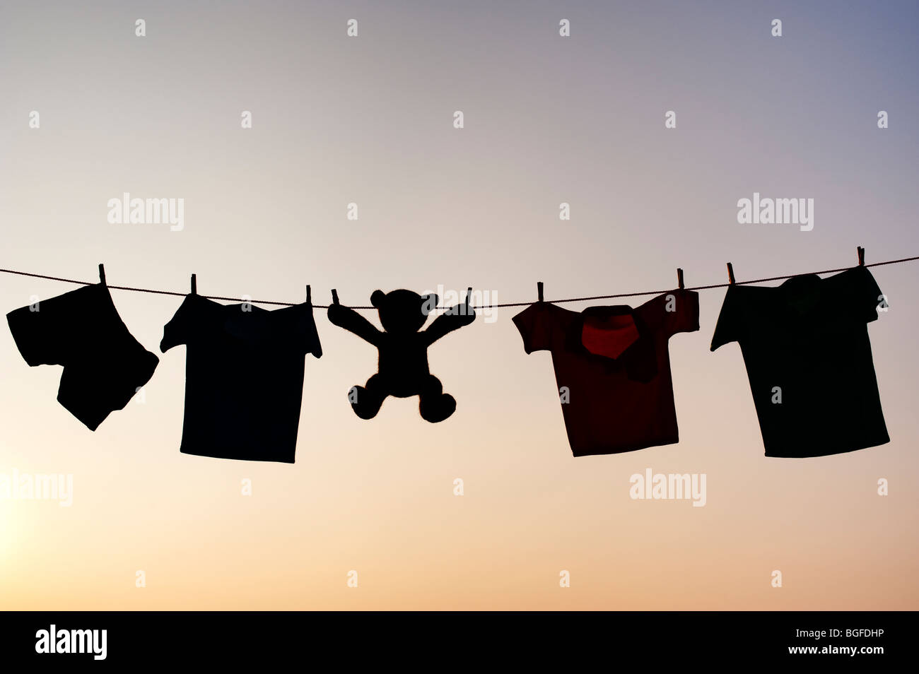 Childrens clothes and teddy bear on a washing line silhouette at dusk. India Stock Photo