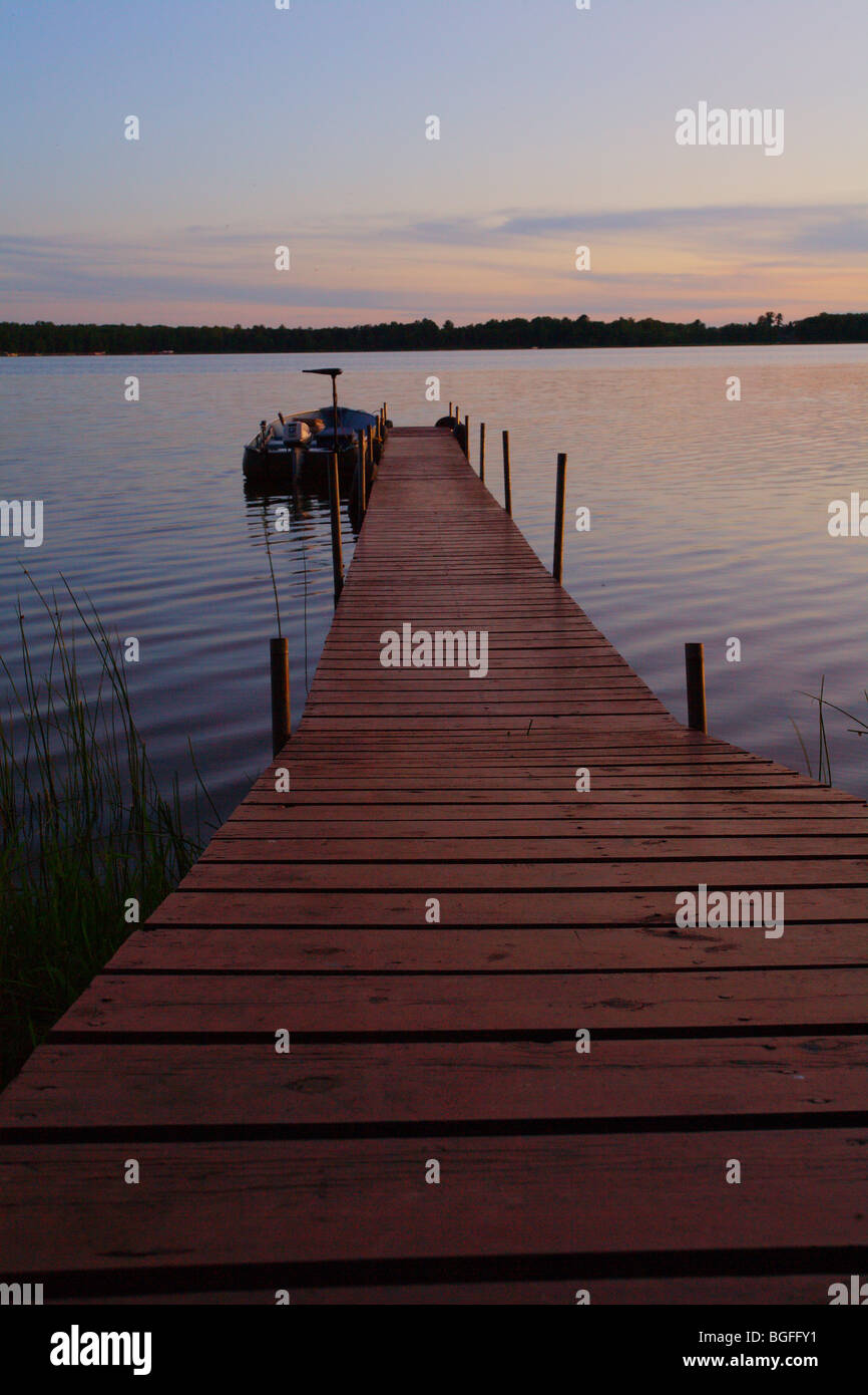 wooden boat ramp leading to boat and boat dock sitting on large fishing lake during sunset Stock Photo
