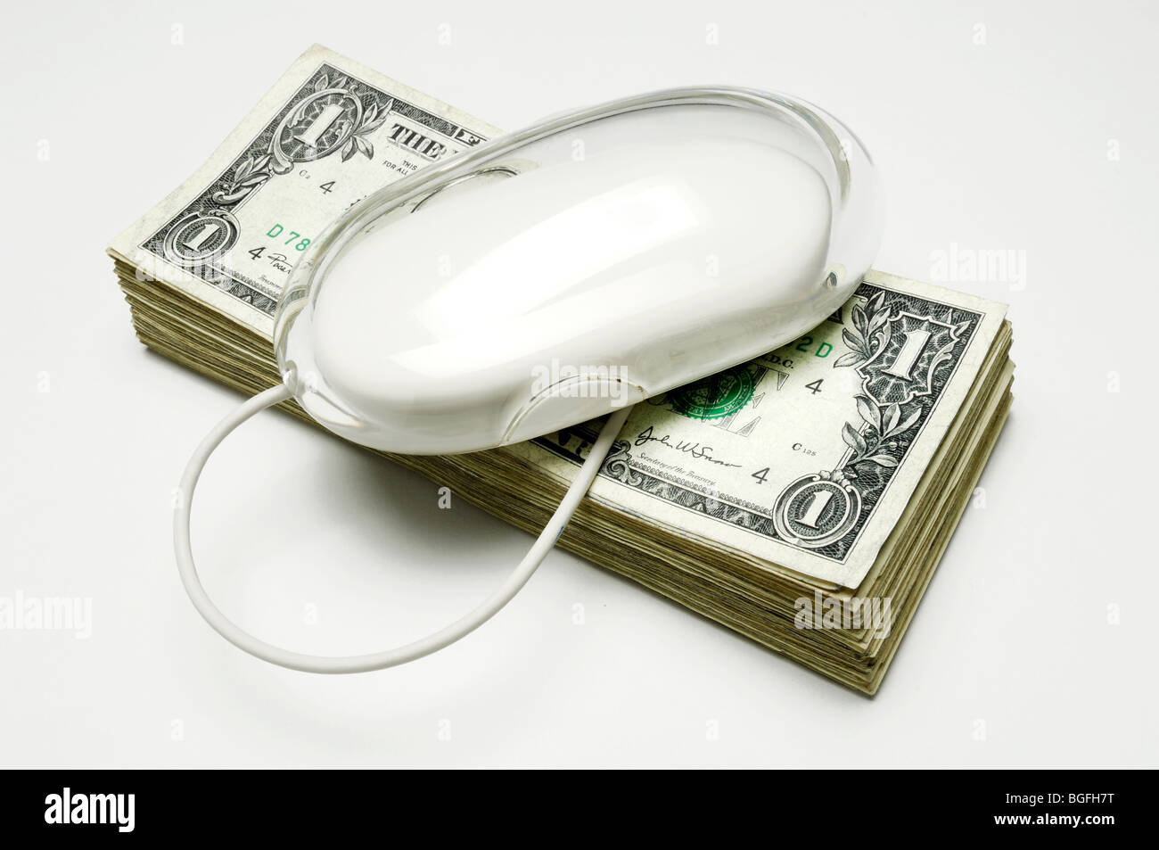 A white computer mouse and cord on a stack of US dollar bills Stock Photo