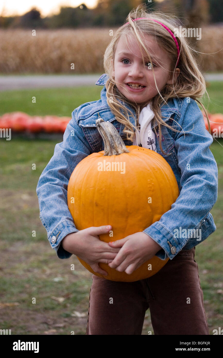 Cute little girl carrying large pumpkin at Halloween time Stock Photo
