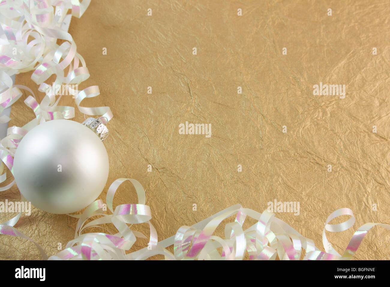 pearl white Christmas ornament with curly metallic ribbon on a textured gold background Stock Photo