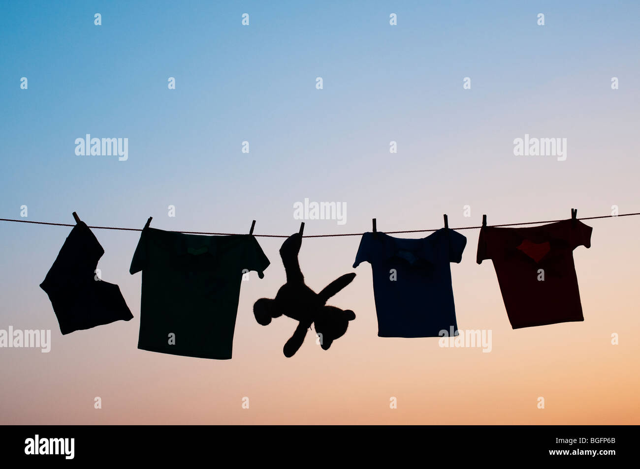 Childrens clothes and teddy bear on a washing line silhouette at dawn. India Stock Photo