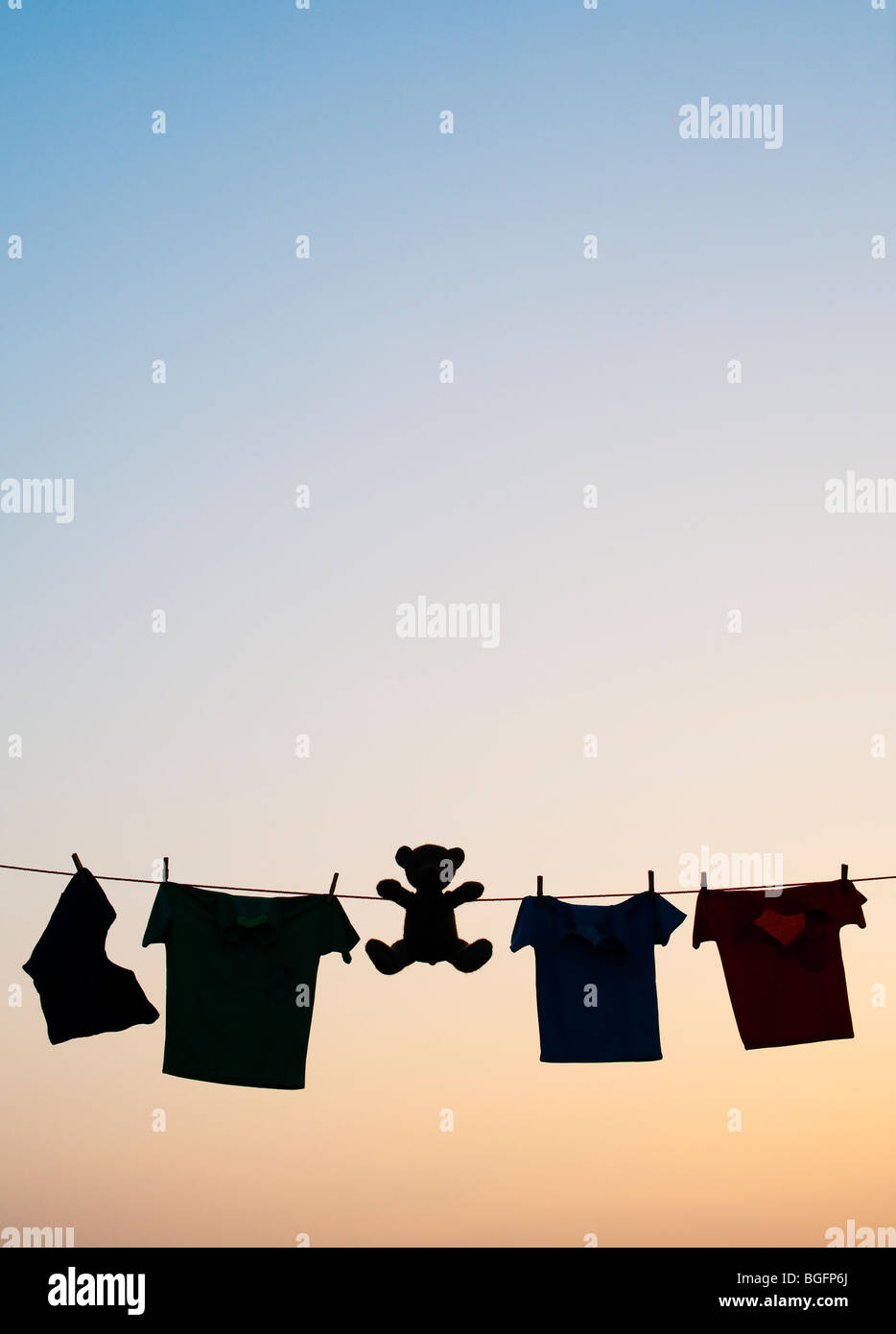 Childrens clothes and teddy bear on a washing line silhouette at dawn. India Stock Photo