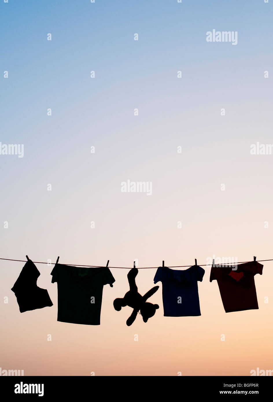 Childrens clothes and teddy bear on a washing line silhouette at dawn. India Stock Photo