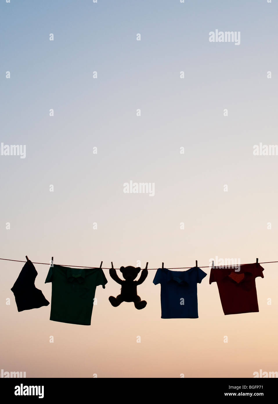 Childrens clothes and teddy bear on a washing line silhouette at dawn. India Stock Photo