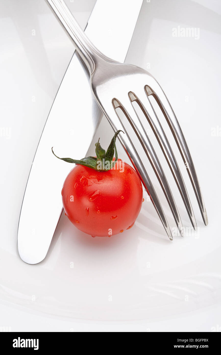 cherry tomato on a plate with fork and knife isolated on white Stock Photo
