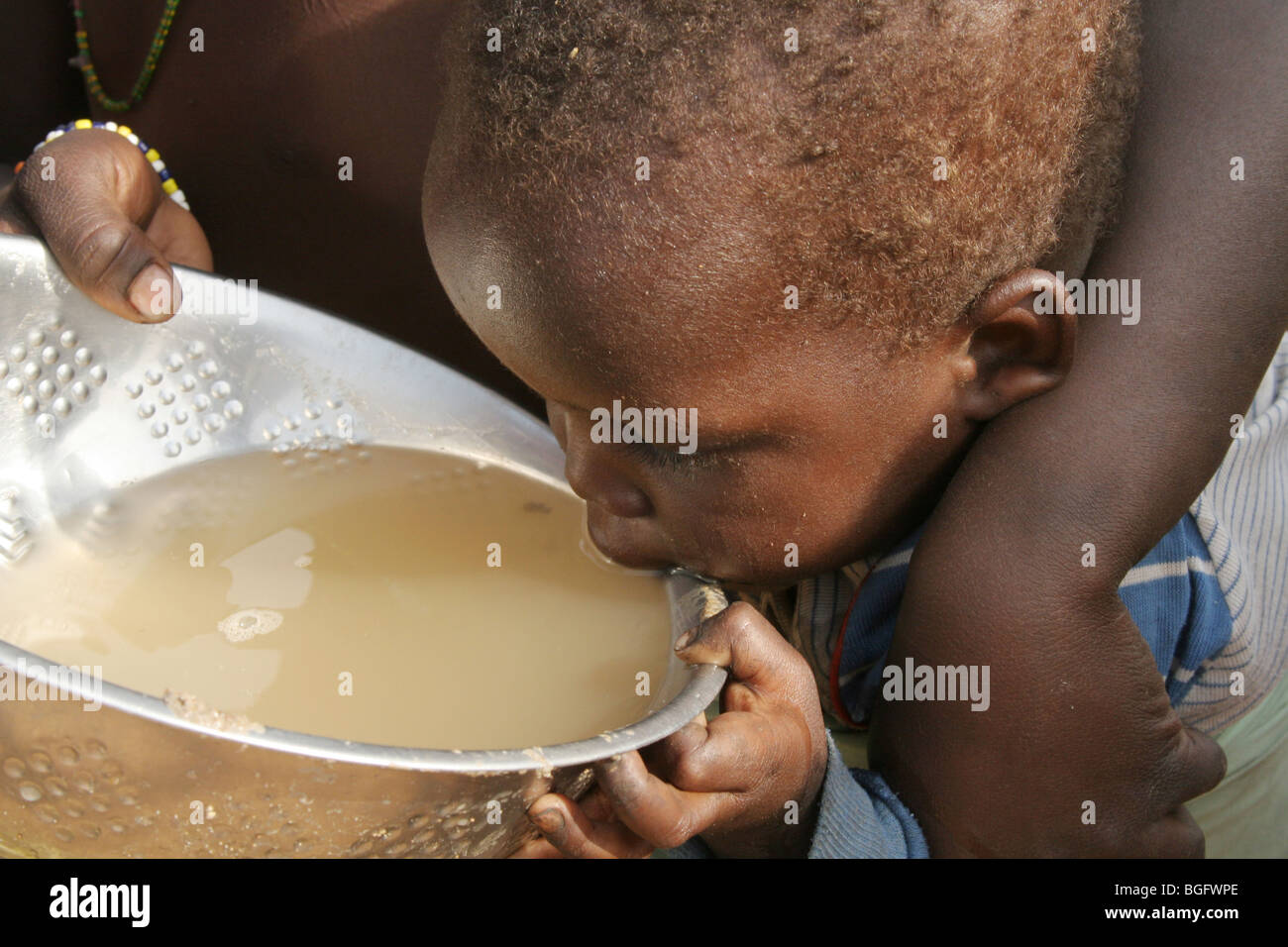 A young child drinking dirty water collected from a dry river bed in Burkina Faso, West Africa Stock Photo