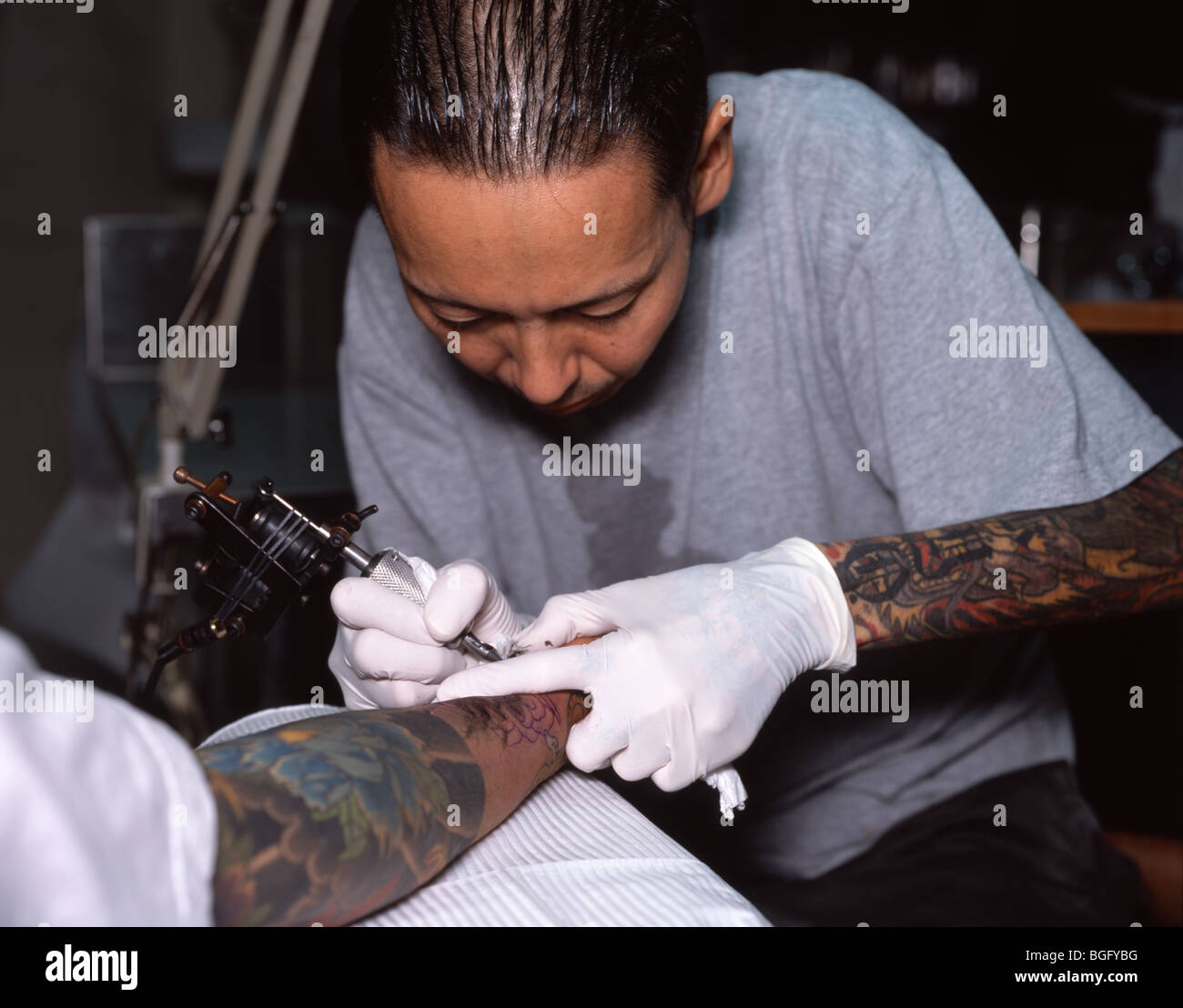 Japanese tattoo artist working on traditional irezumi on clients arm. Stock Photo