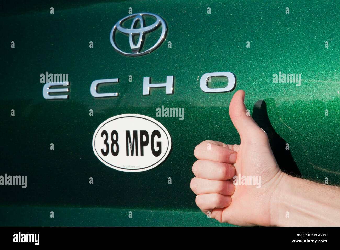 Close up of person holding thumbs up next to 38 miles per gallon fuel efficiency bumper sticker on green Toyota Echo car. Stock Photo