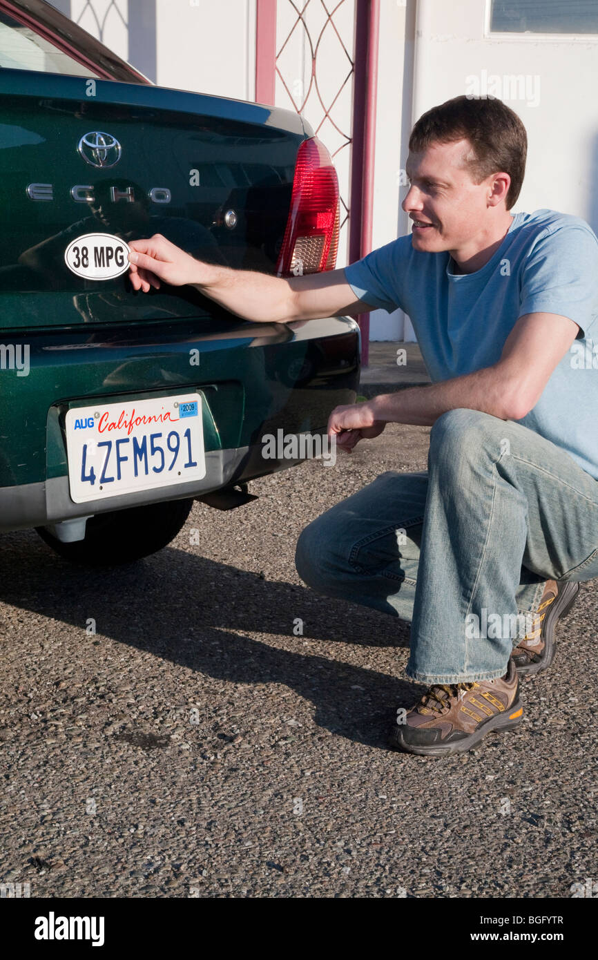 Mid adult man placing a 38 miles per gallon fuel efficiency bumper sticker installed on Toyota Echo car. California, USA Stock Photo