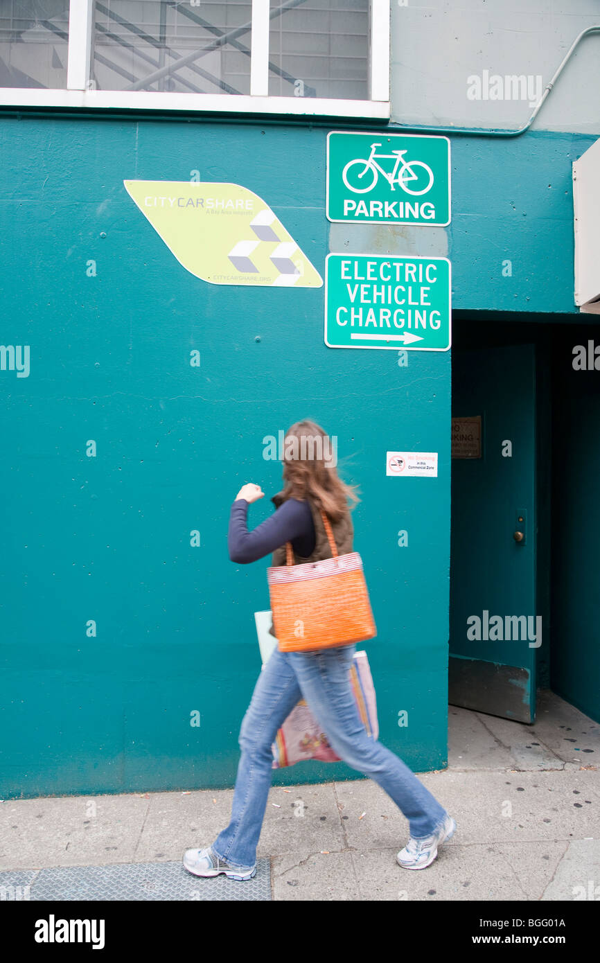 Woman walking by City CarShare (car rental service), bicycle parking, and electric vehicle charging station signs. Stock Photo