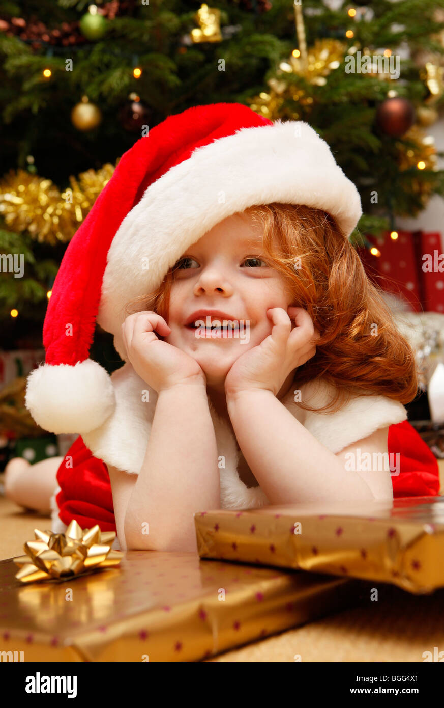 Girl, Children with presents by the Christmas Tree. Dressed as Santa, Father Christmas. Stock Photo