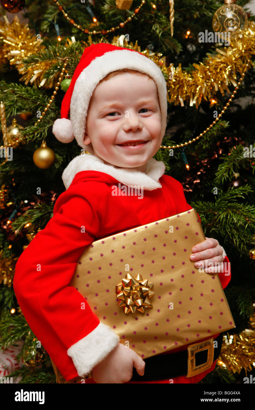 Little boy dressed up as father christmas with presents and tree Stock