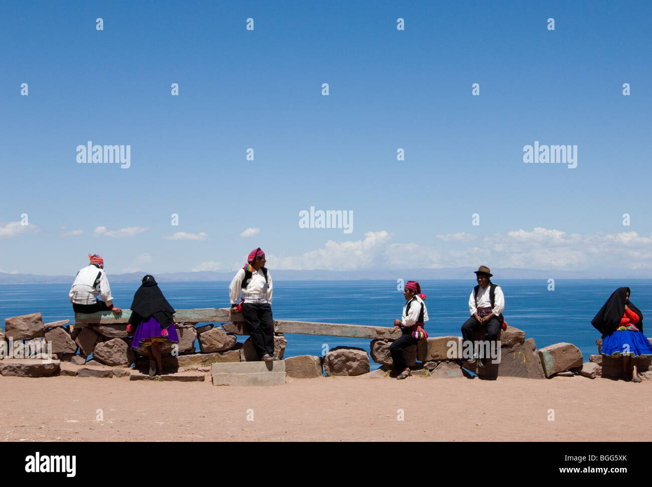 Men & Women of Taquile Island sitting on wall in traditional clothes overlooking Lake Titicaca Stock Photo