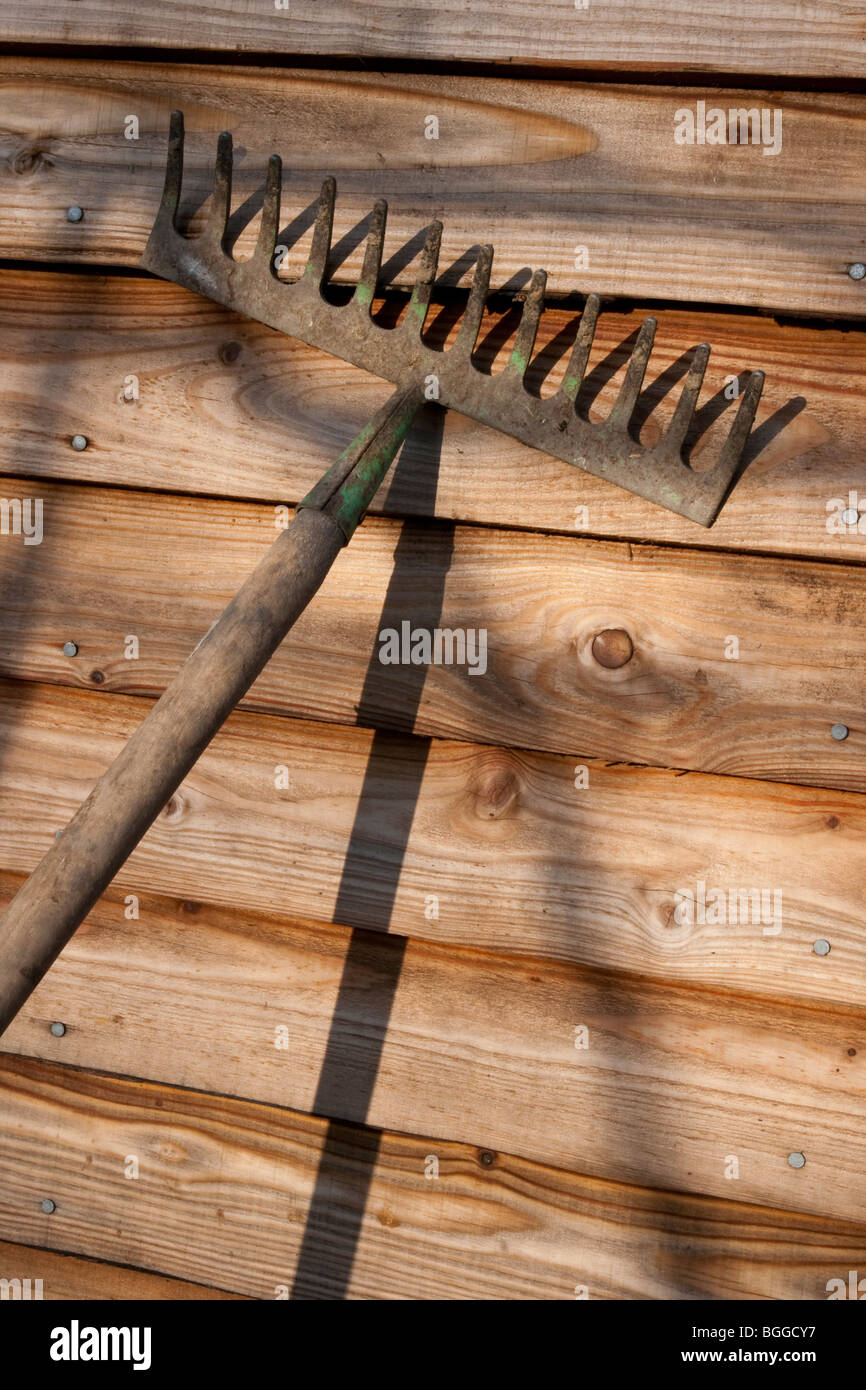 Old garden rake leaning against a shed wall Stock Photo 