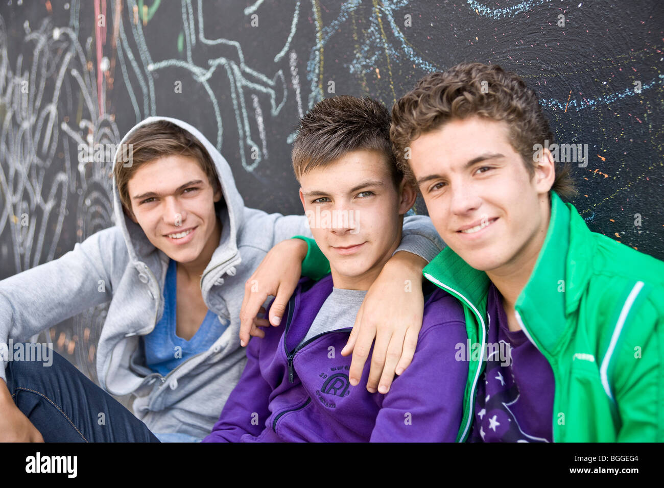 Three boys sitting side by side in front of a wall, close-up Stock Photo