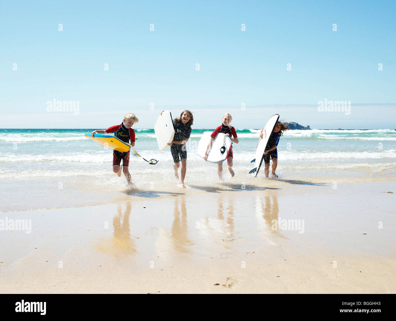 Children with surfboards running out of the water, front view Stock Photo