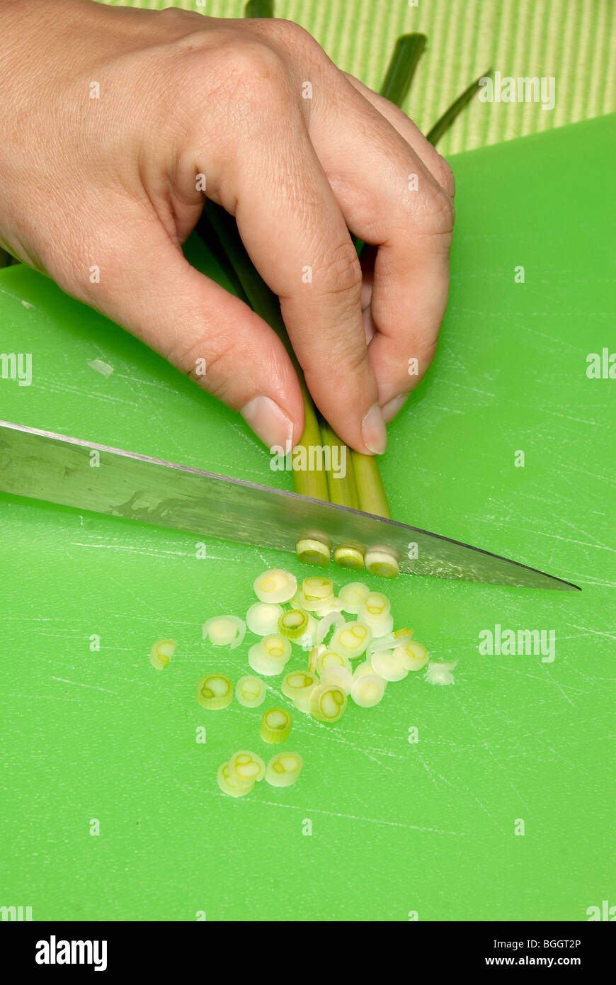 A chef dices green onions into small, chopped slices on a green cutting ...