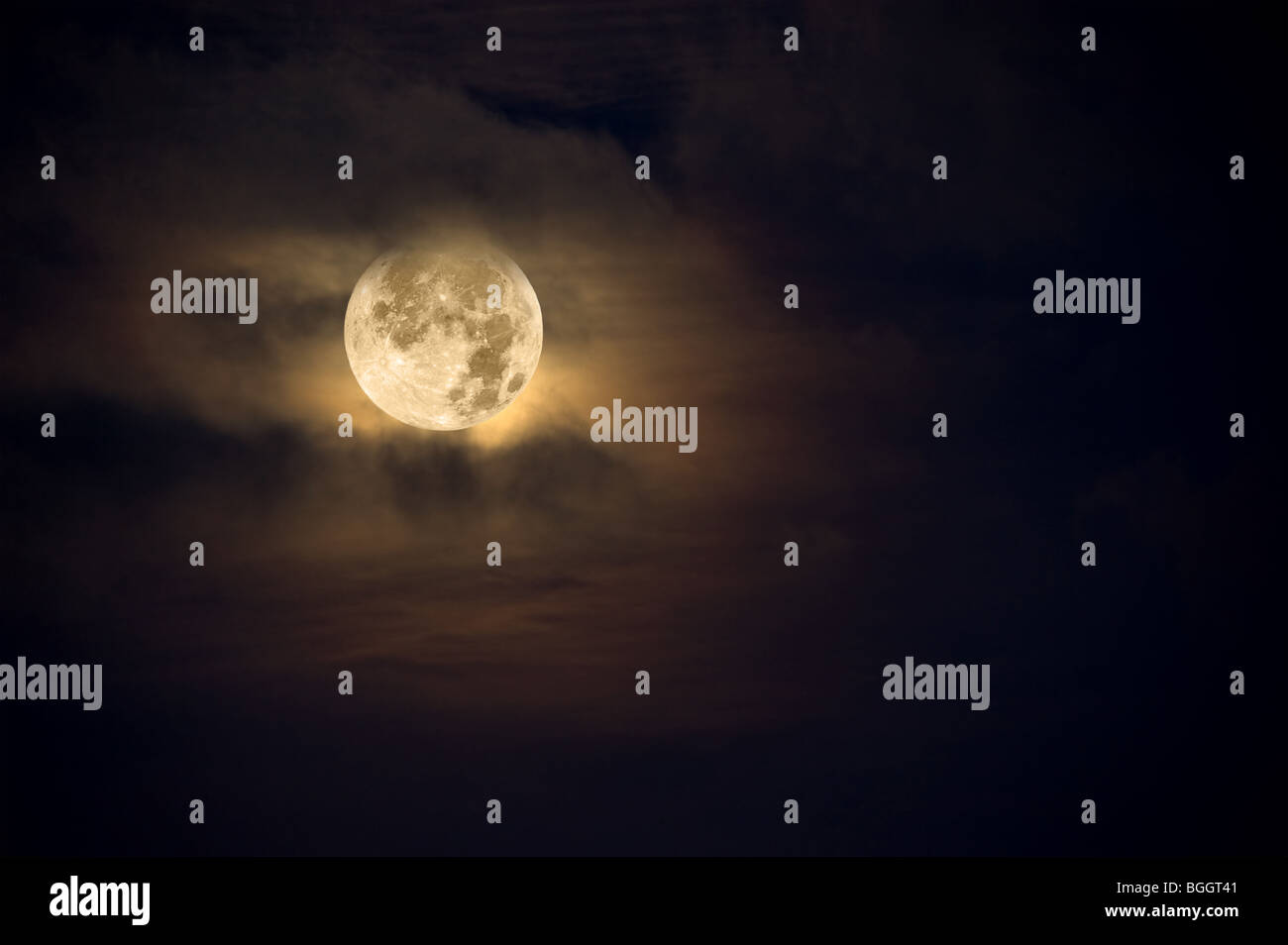 A dark night brings a bright, amber moon alive with puffy hazy clouds. Stock Photo