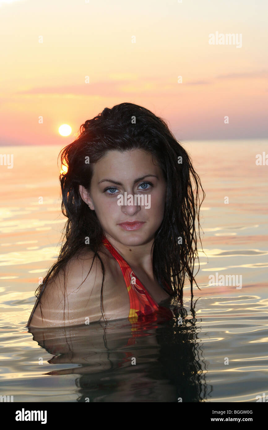 Attractive girl up to her shoulders in beautiful, sparkling water created by the setting sun Stock Photo