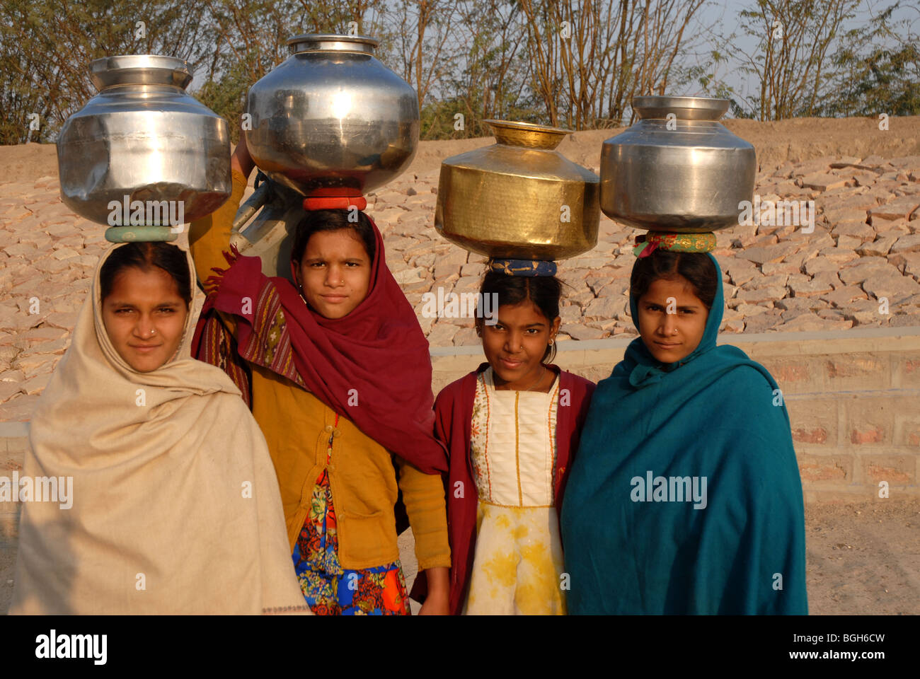 4 (four) Rajasthani girls carring water jugs on their heads on their way to the village well looking at camera Stock Photo