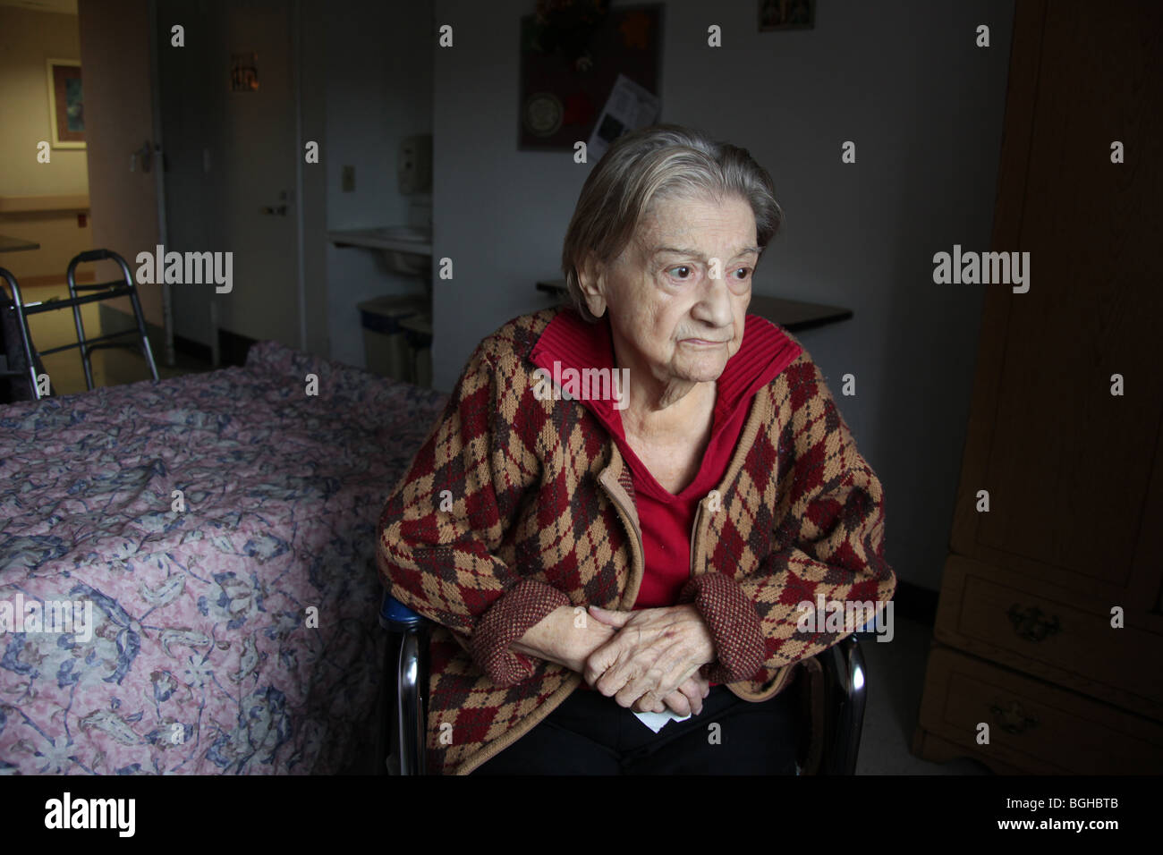 Elderly woman sits in her room at a nursing home, lost in thought. Stock Photo