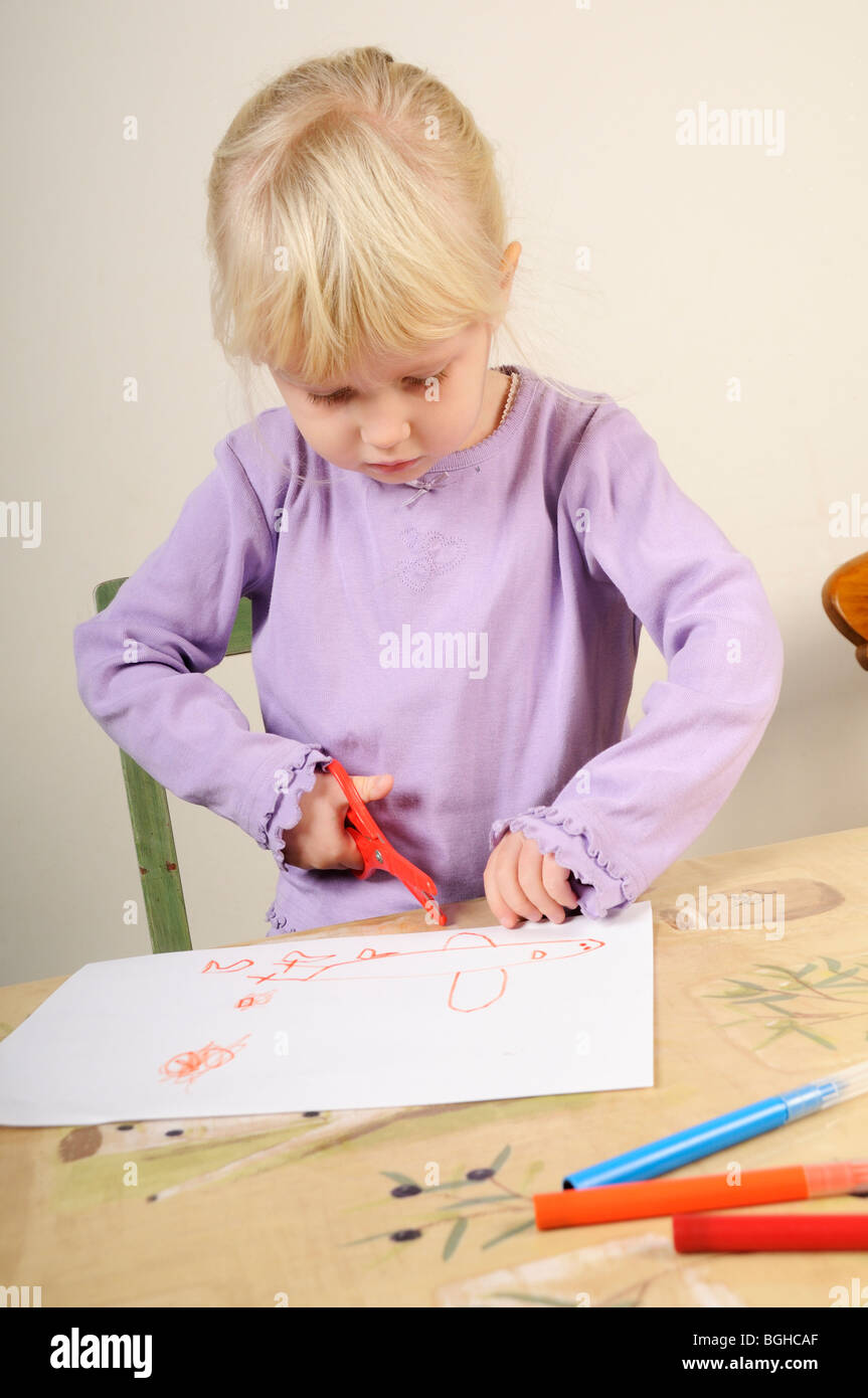 Stock photo of a four year old girl cutting out a picture she has just drawn on a piece of paper. Stock Photo