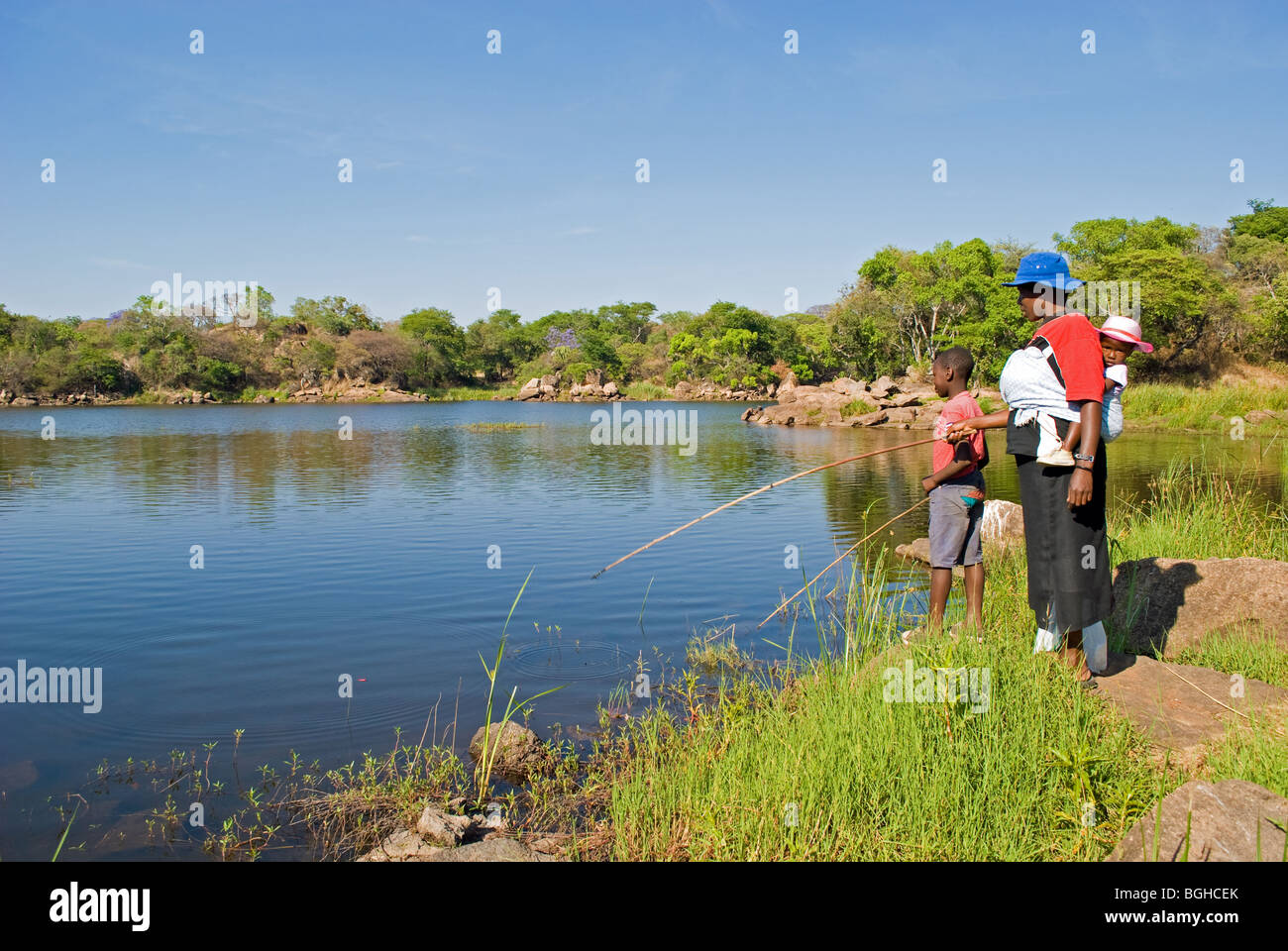 A mother and her two children fish for food at Hillside Dams in Bulawayo, Zimbabwe. Stock Photo