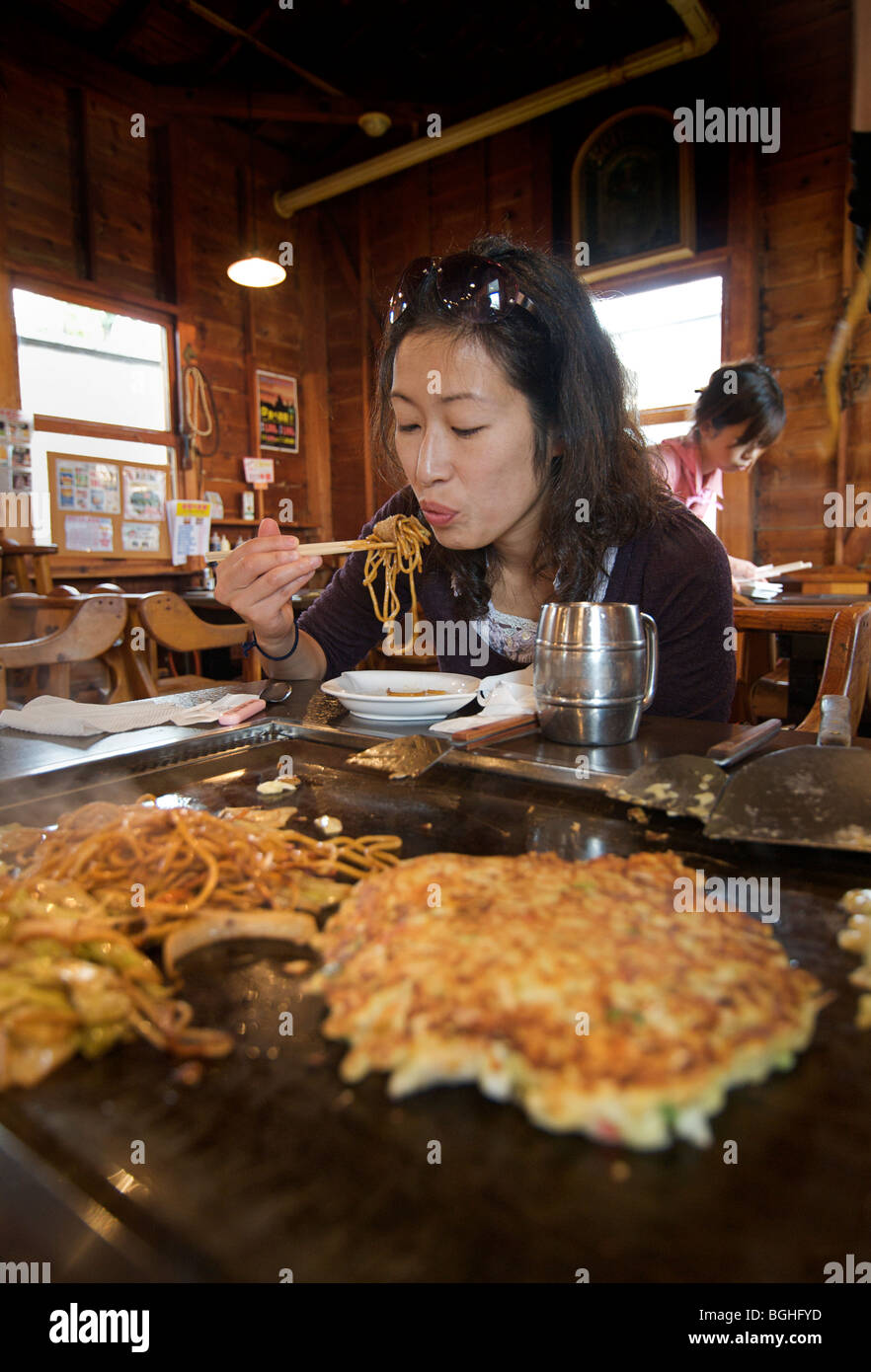 Okonomi yaki. Japanese style savoury pancakes. Japanese woman eating noodles Japan Stock Photo