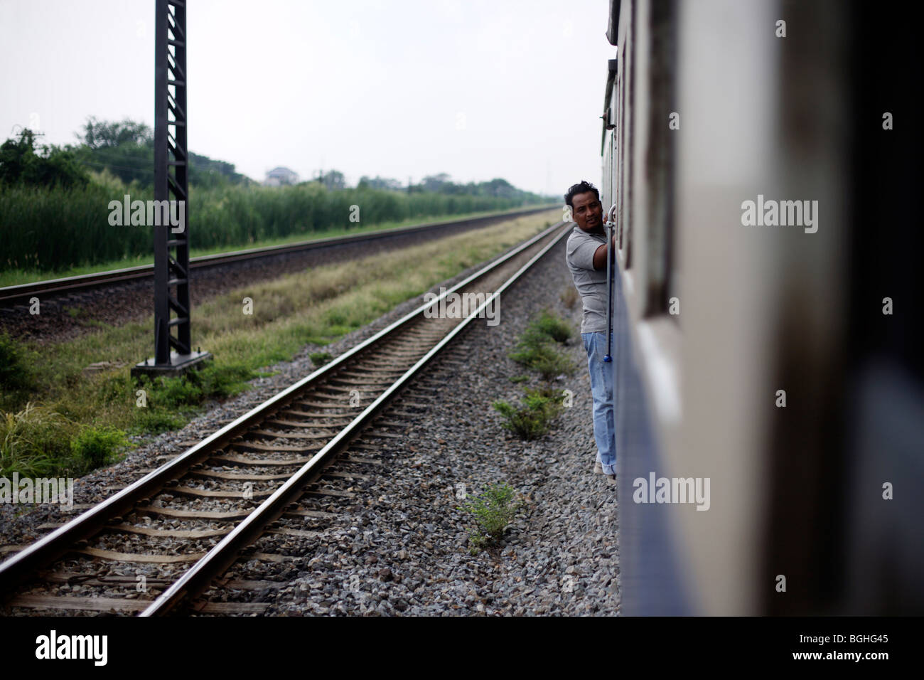 A man stands between carriages on a train in motion in Thailand Stock Photo