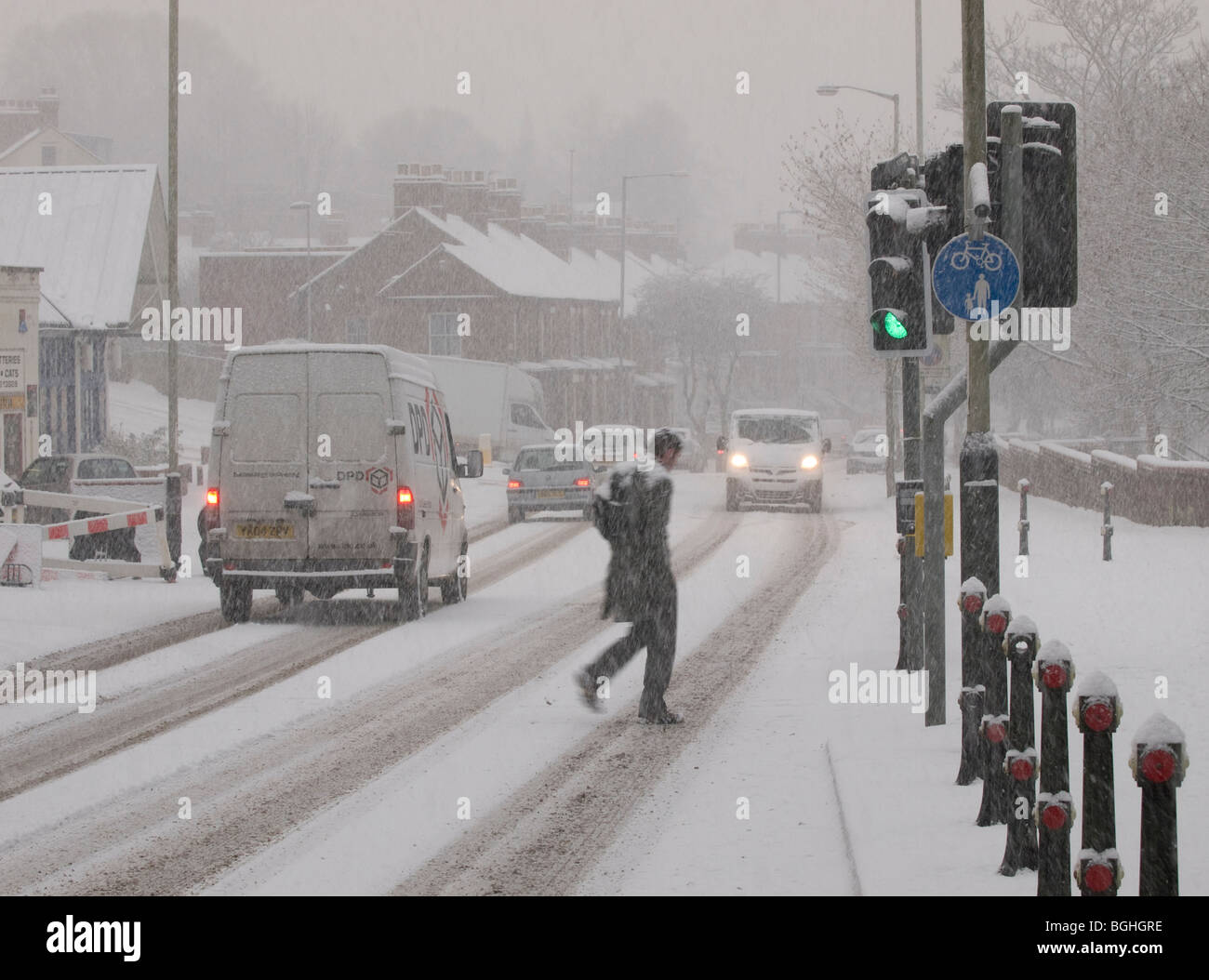 MAN CROSSING ROAD AT ZEBRA PEDESTRIAN WITH TRAFFIC IN THE SNOW ON RIVERSIDE ROAD NORWICH NORFOLK EAST ANGLIA ENGLAND UK Stock Photo