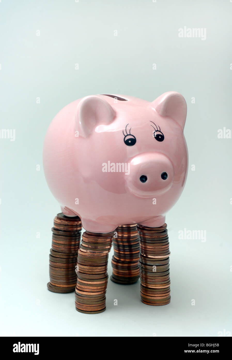 PIGGYBANK,PIGGYBANKS STANDING ON PILES OF BRITISH COINS RE THE ECONOMY SAVINGS INCOMES THE RECESSION BANKS CASH WAGES UK Stock Photo