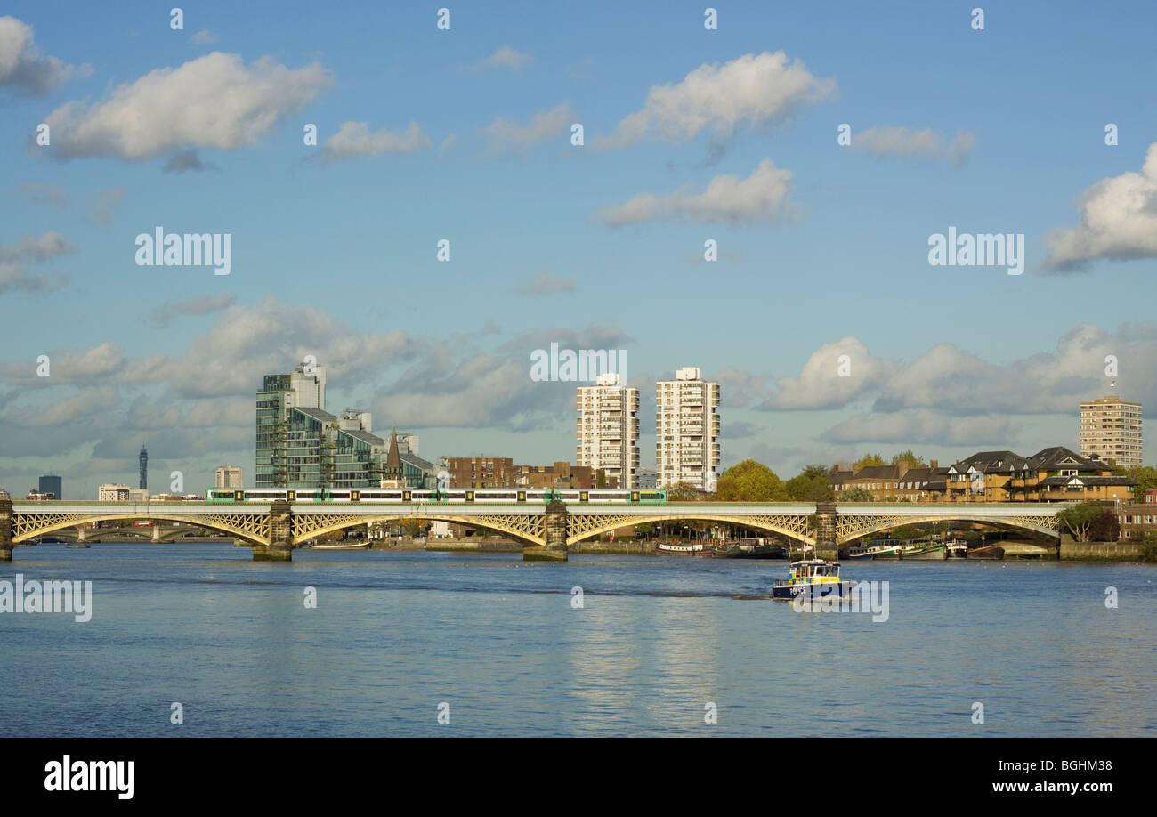 Train crossing over the river Thames via the Battersea Railway Bridge with a Police boat in the foreground. Stock Photo