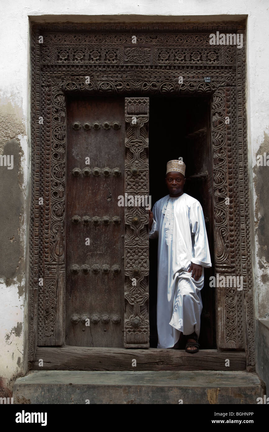Stone Town, Zanzibar, Tanzania.  An African Zanzibari Wearing Traditional Kanzu and Kofia (Hat) Stands in the Doorway. Stock Photo