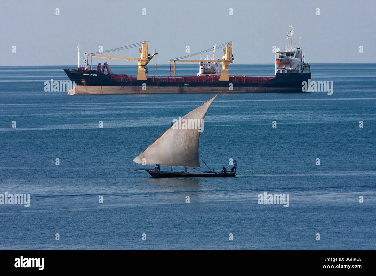 Zanzibar, Tanzania. Juxtaposition of Two Eras.  Cargo Freighter and Traditional Dhow Share the Harbor in Zanzibar. Stock Photo