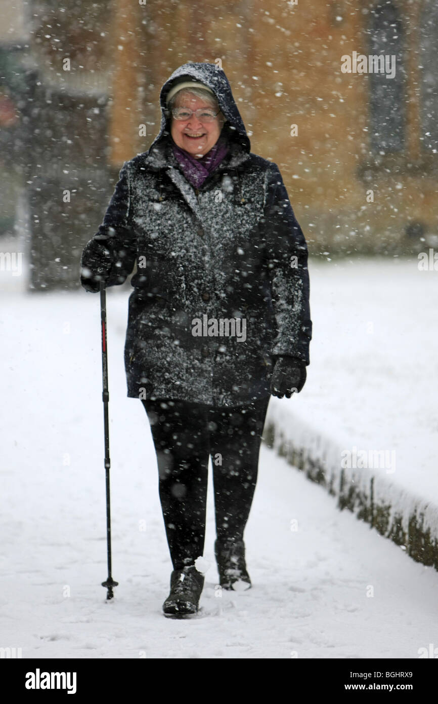 Elderly woman walking through a snow storm carries a hiking pole as an ...