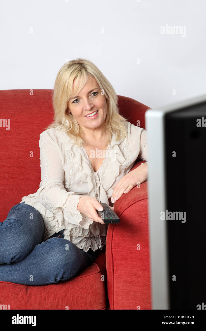 Happy blonde woman sitting watching tv holding a remote control Stock Photo