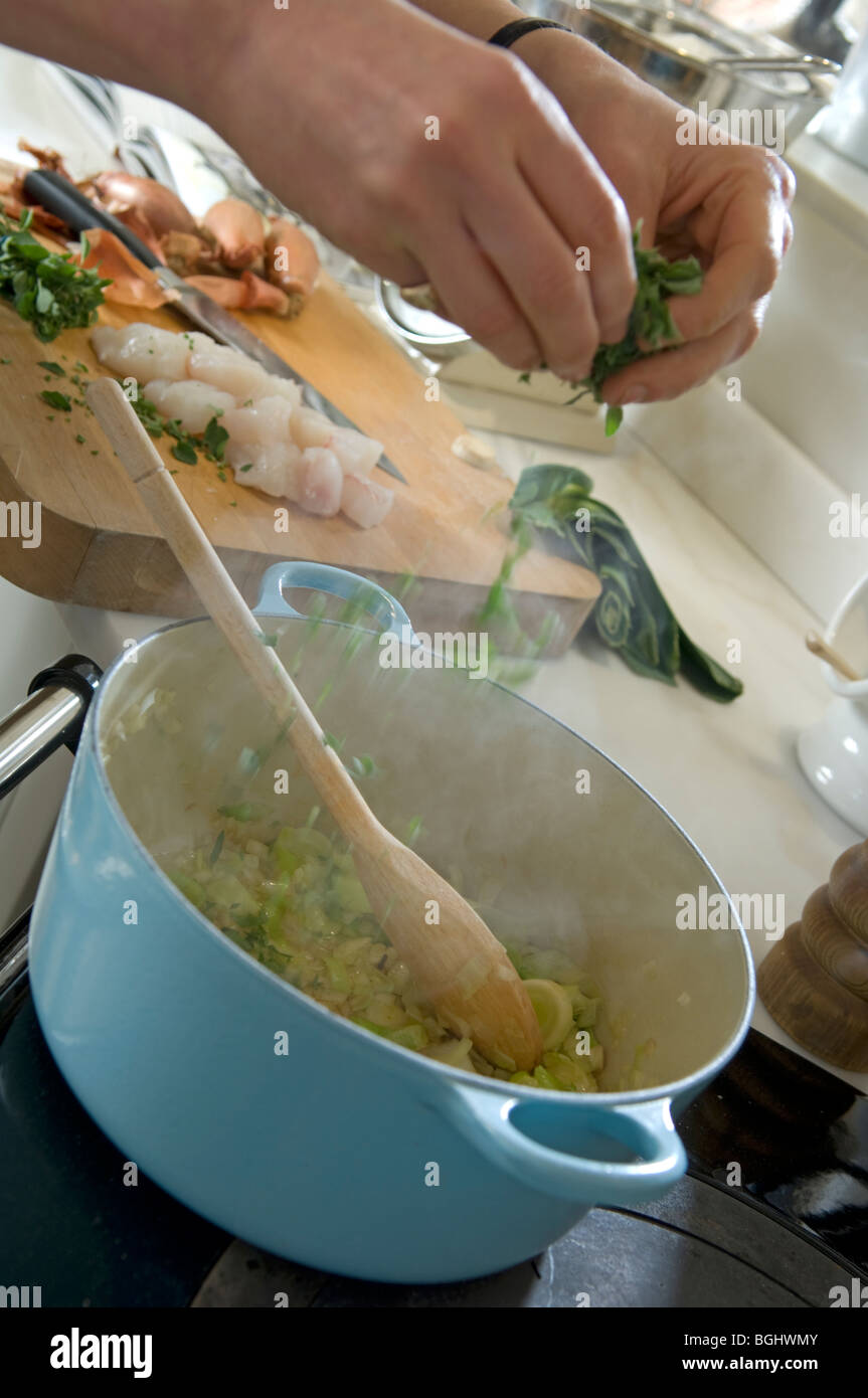 Adding herbs to casserole dish on stove top Stock Photo